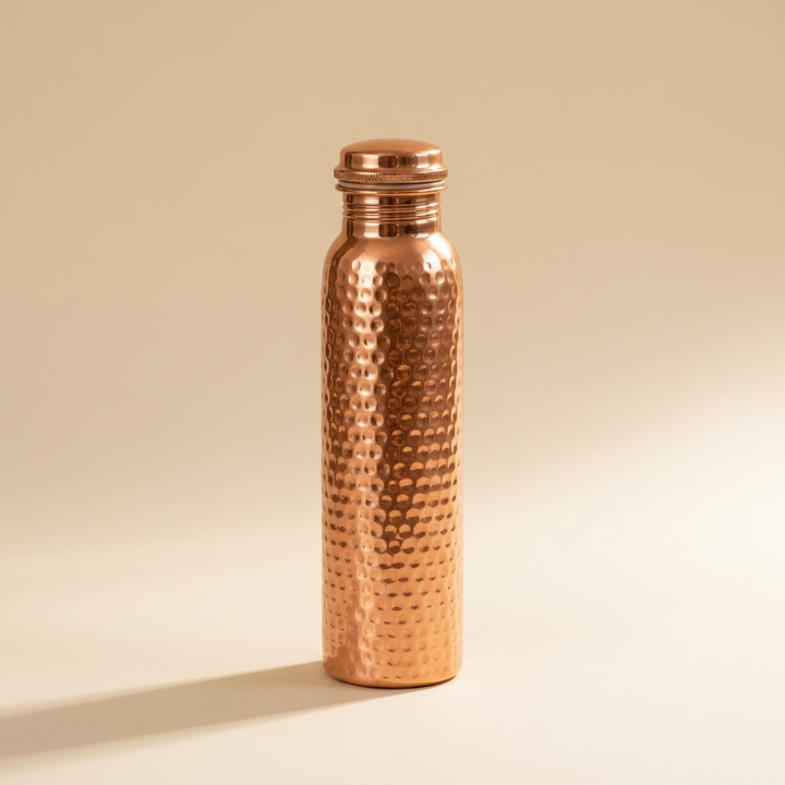 Hammered copper water bottle with screw-top lid on a warm off-white background